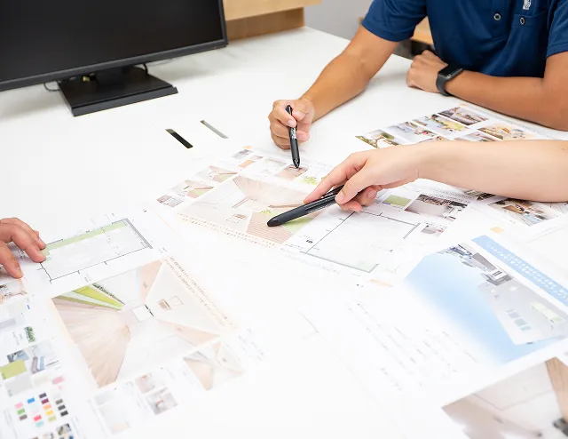 改修計画に合わせた2つの提案書のイメージの写真。2人の人物が図面にメモをしている様子の手元が写っている。