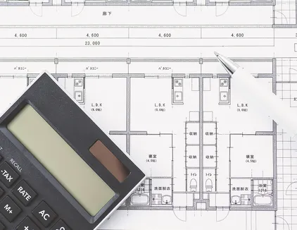 予算管理のイメージ写真。図面の上に電卓とペンが置かれている。